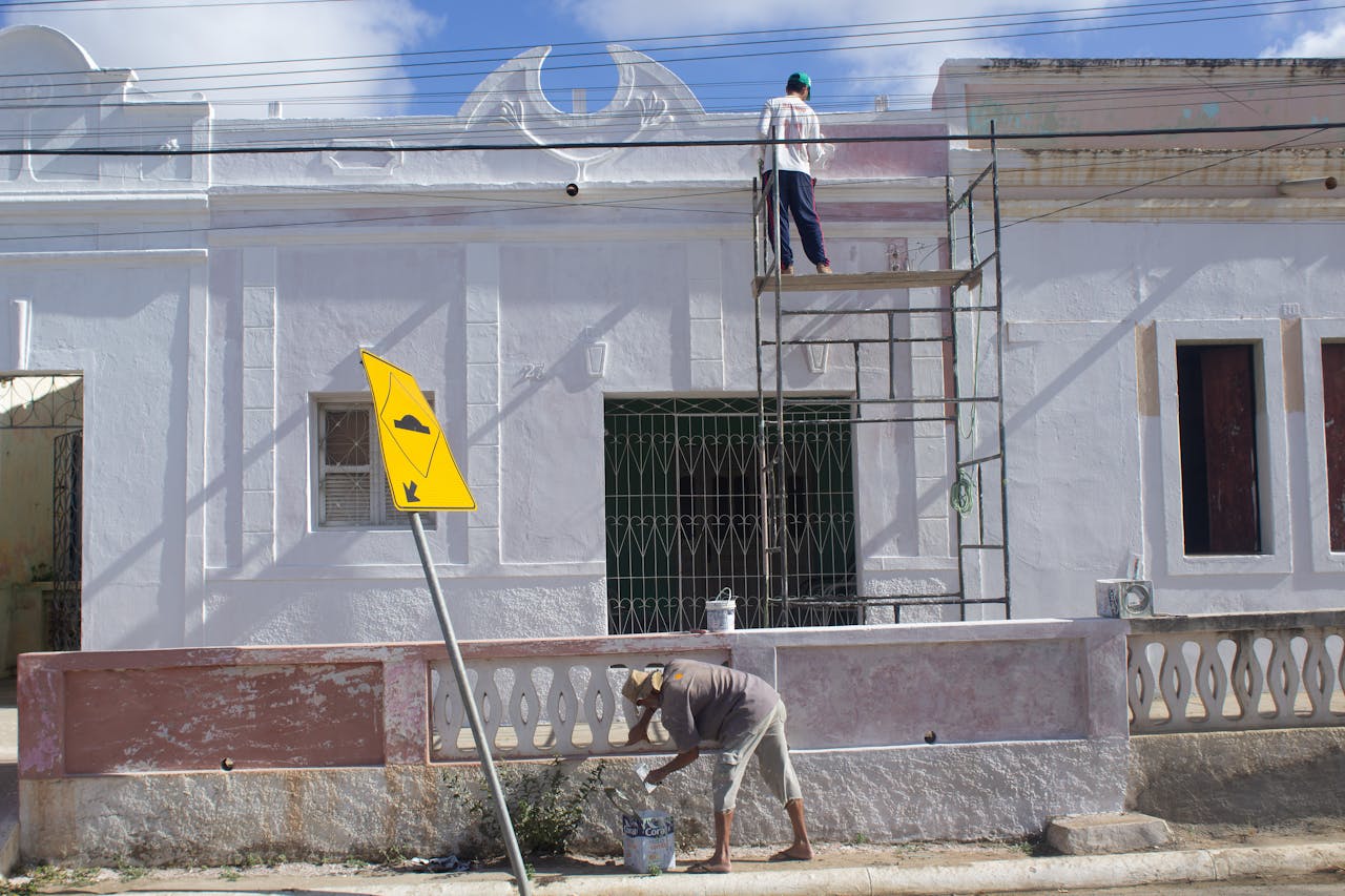 Contact Two men working on a building facade renovation with scaffolding and street sign.