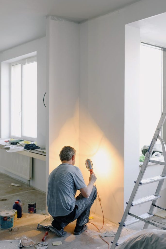 Home Back view of anonymous male in dirty clothes renovating walls in home while holding lamp